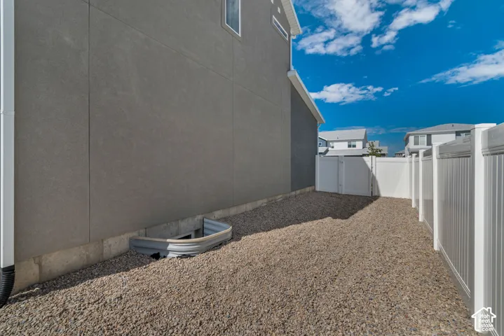 Gravel side yard featuring a vinyl privacy fence, and a window well
