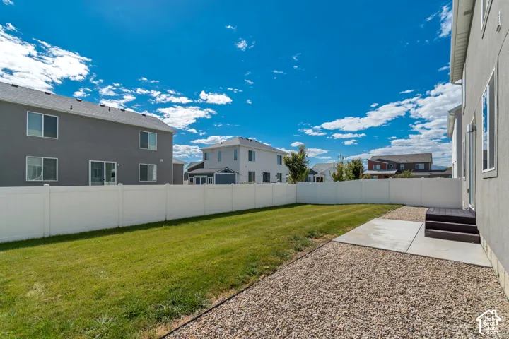 Manicured lawn, white privacy fence, concrete patio, gravel landscaping, and exterior stairs