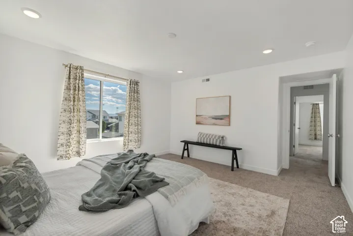 Recessed ceiling lighting, white walls, carpeted flooring, and a window with a neighborhood backdrop