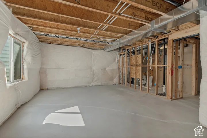 Unfinished basement featuring exposed wood framing, concrete flooring, visible ductwork, and a framed window opening
