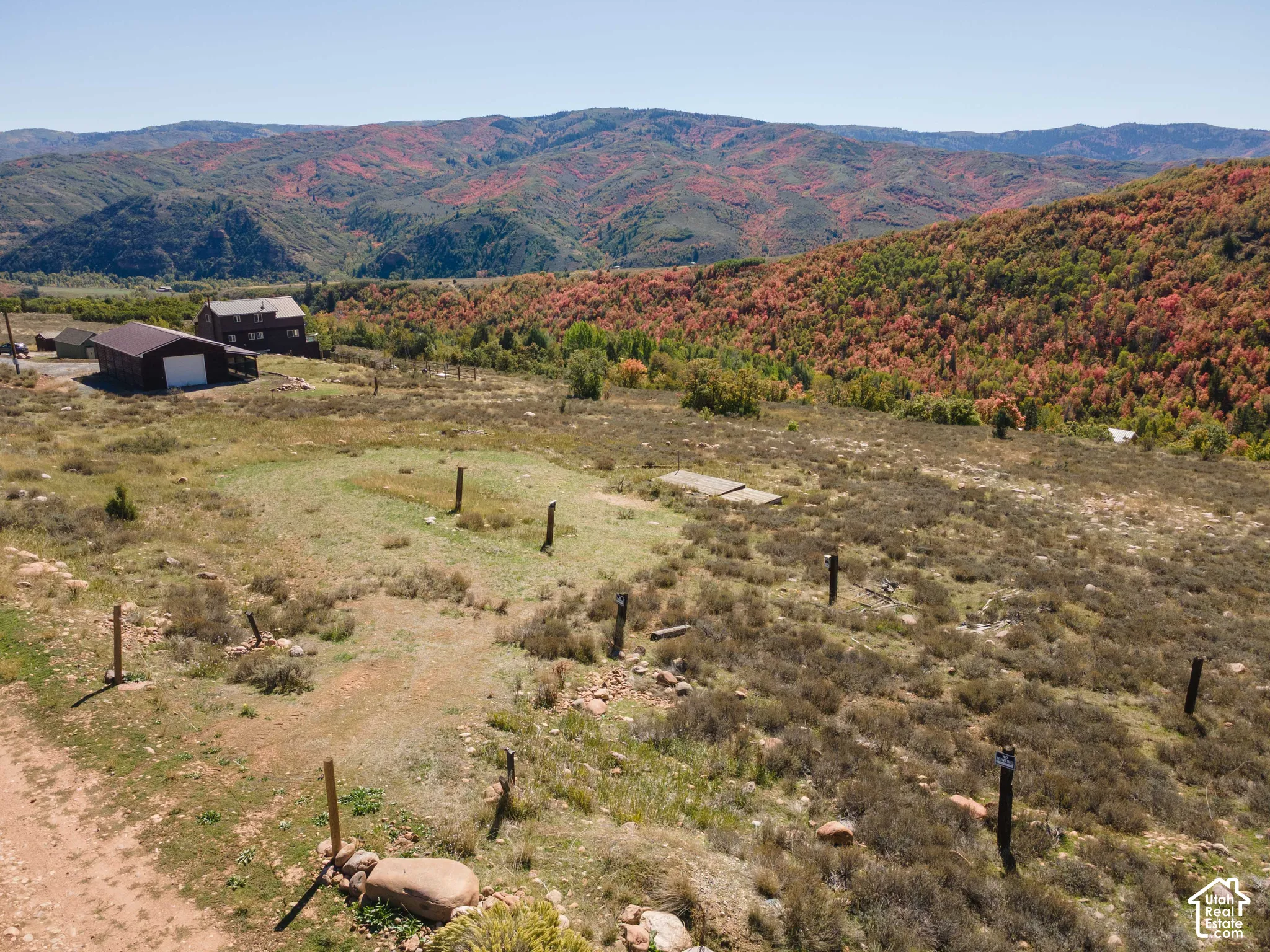 Expansive property featuring a rustic-style residence, an outbuilding with a garage door, and a mountainous backdrop with varied foliage