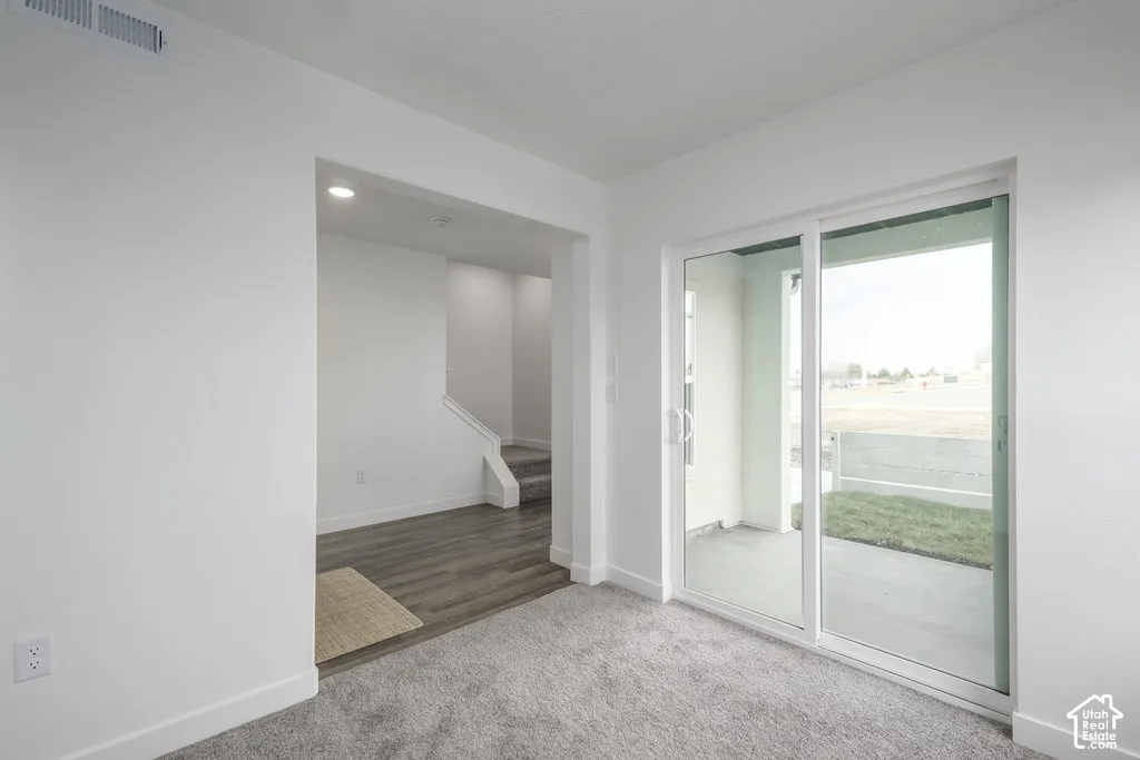 Sliding glass door leading to a concrete patio, light gray carpet, recessed lighting, wood-finish flooring, and a carpeted staircase