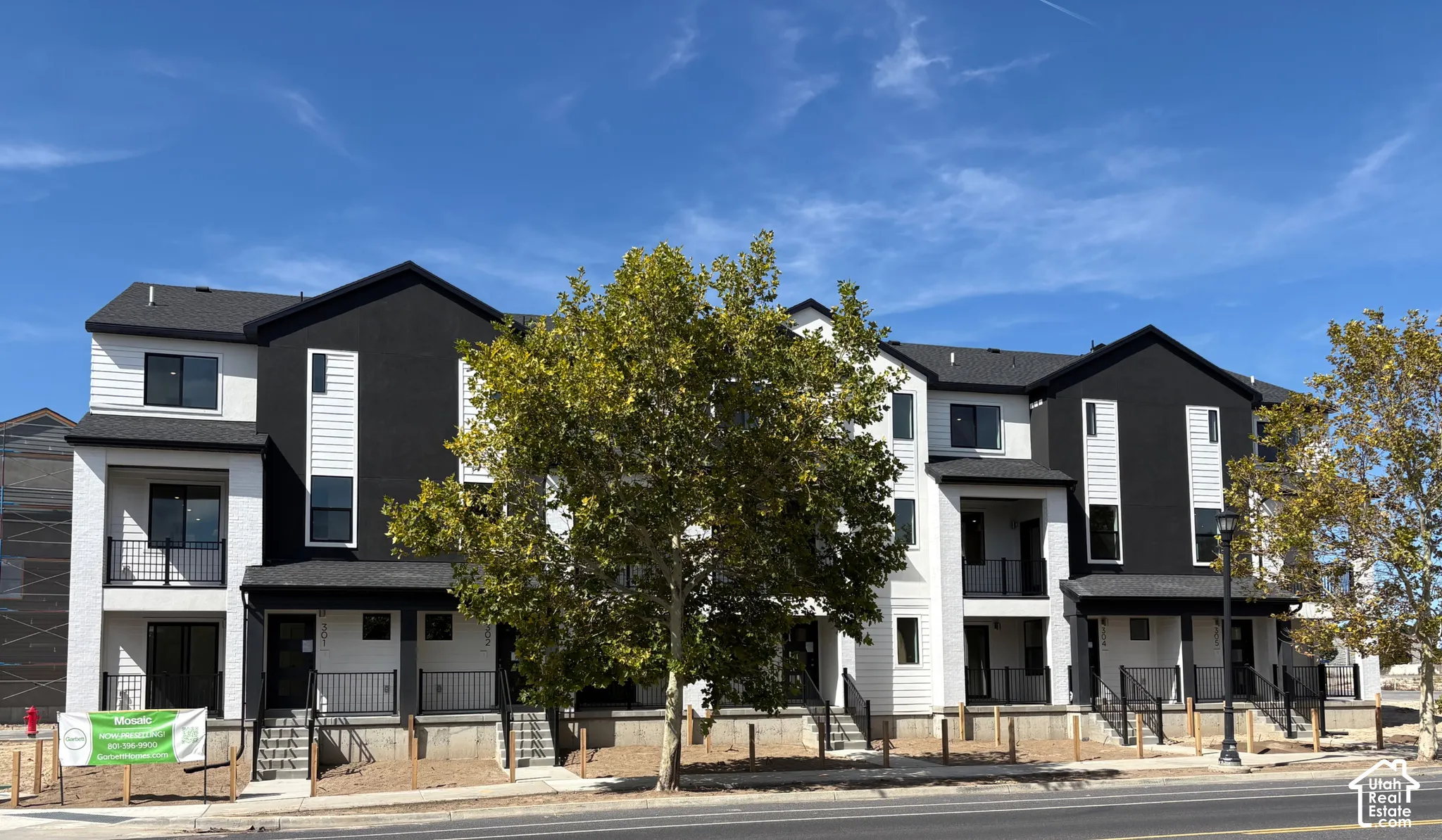 Modern multi-story facade featuring dark-framed windows, white horizontal siding, dark vertical accents, and private balconies