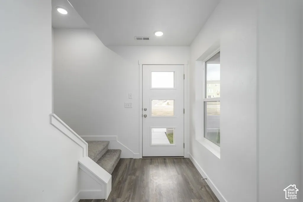 Wood-finish flooring, recessed lighting, white walls, modern front door with frosted glass panels, and a large window