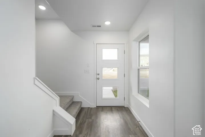 Wood-finish flooring, recessed lighting, white walls, modern front door with frosted glass panels, and a large window