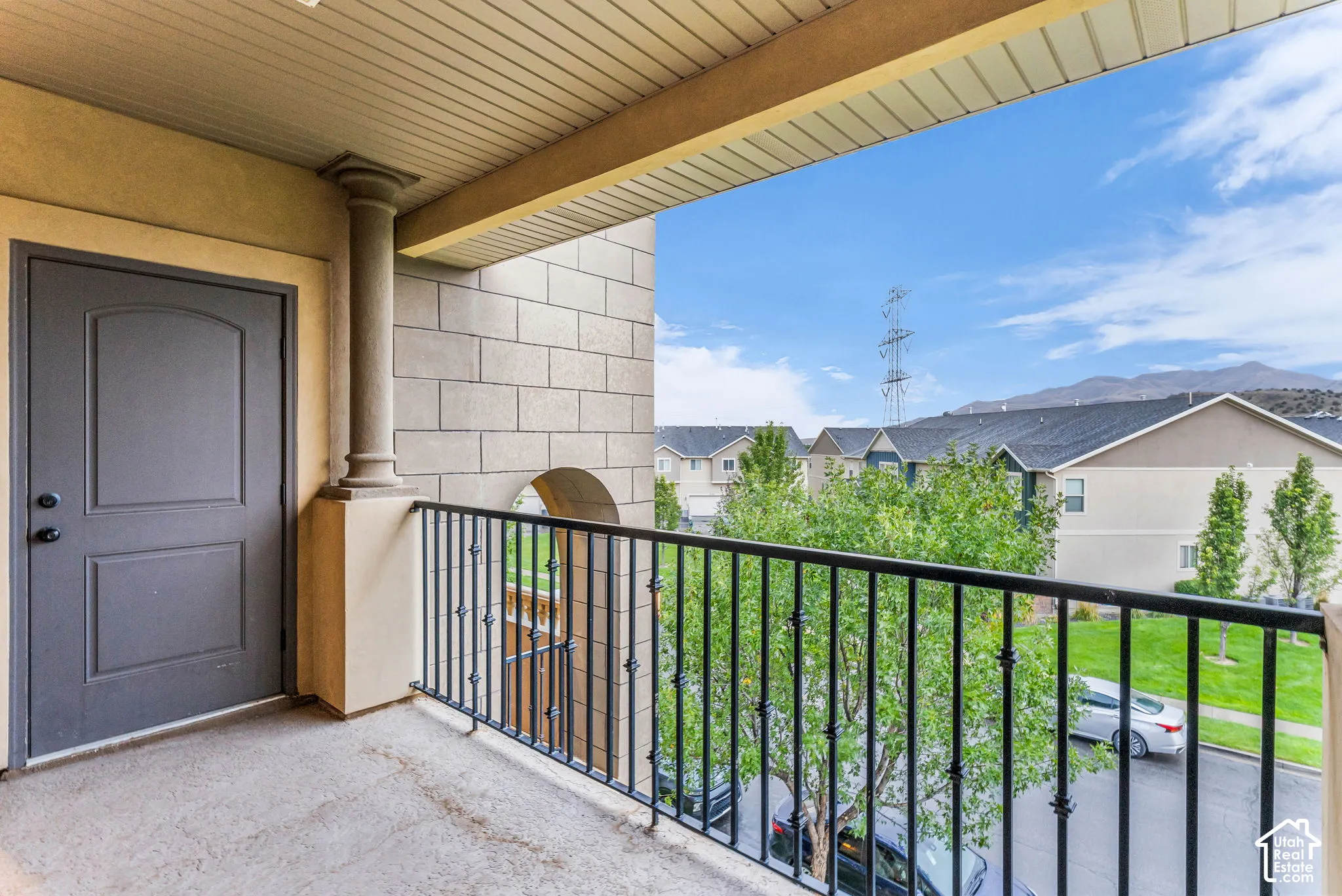 Private balcony with concrete flooring, black wrought iron railing, and decorative stone column