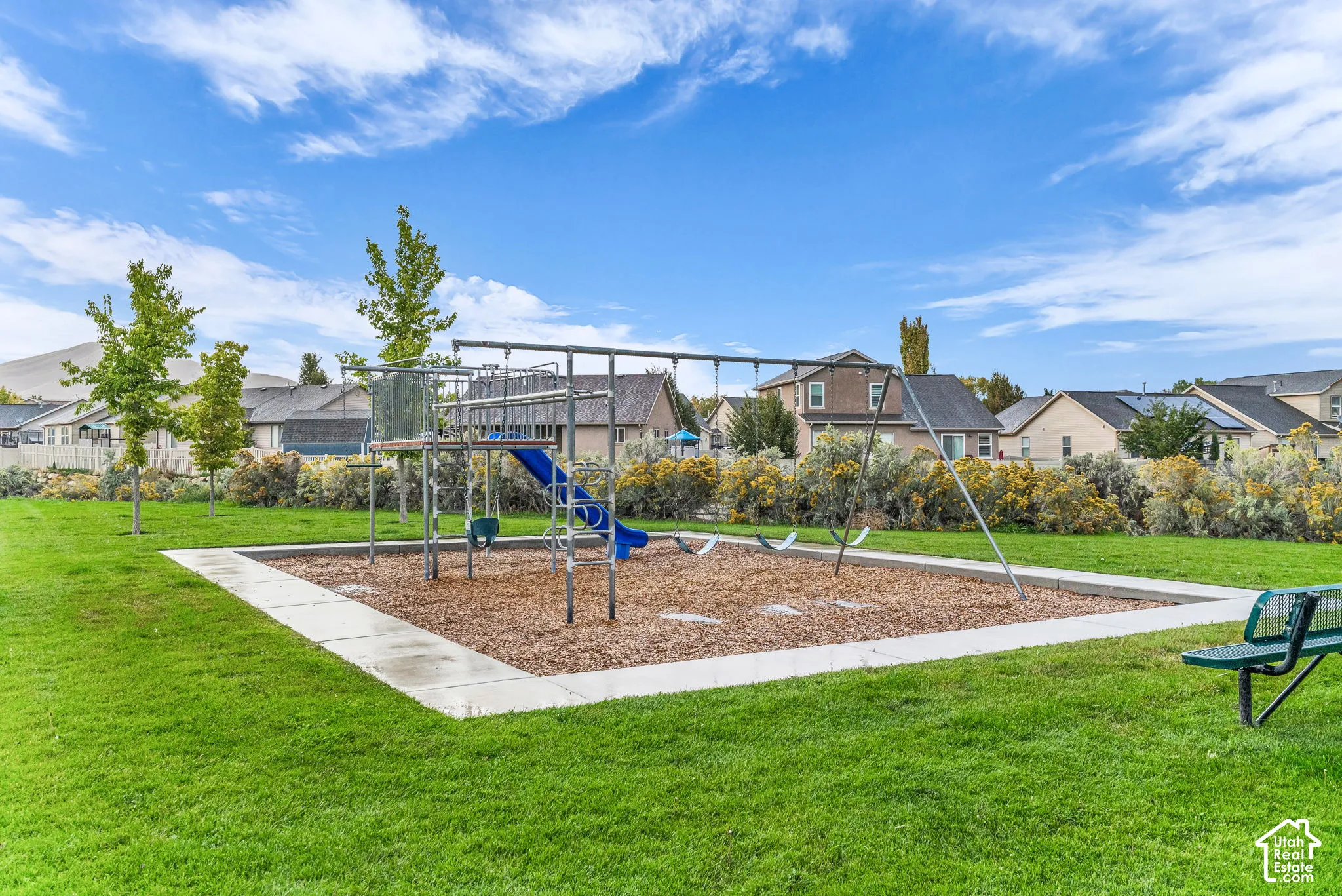 Community playground area featuring a play structure with a slide and swings, surrounded by a green lawn