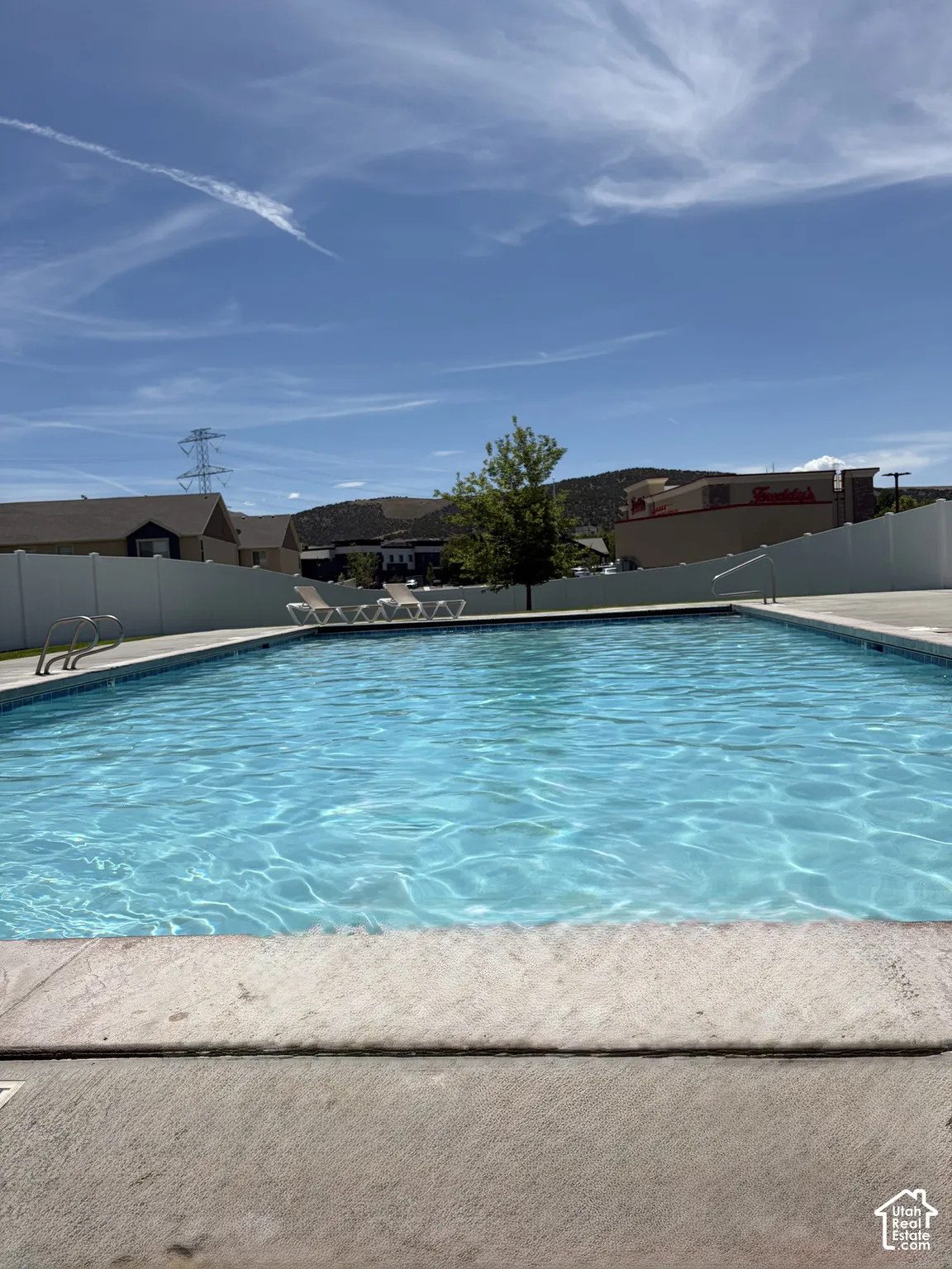 Outdoor swimming pool with concrete decking, white privacy fencing, and distant hillside scenery