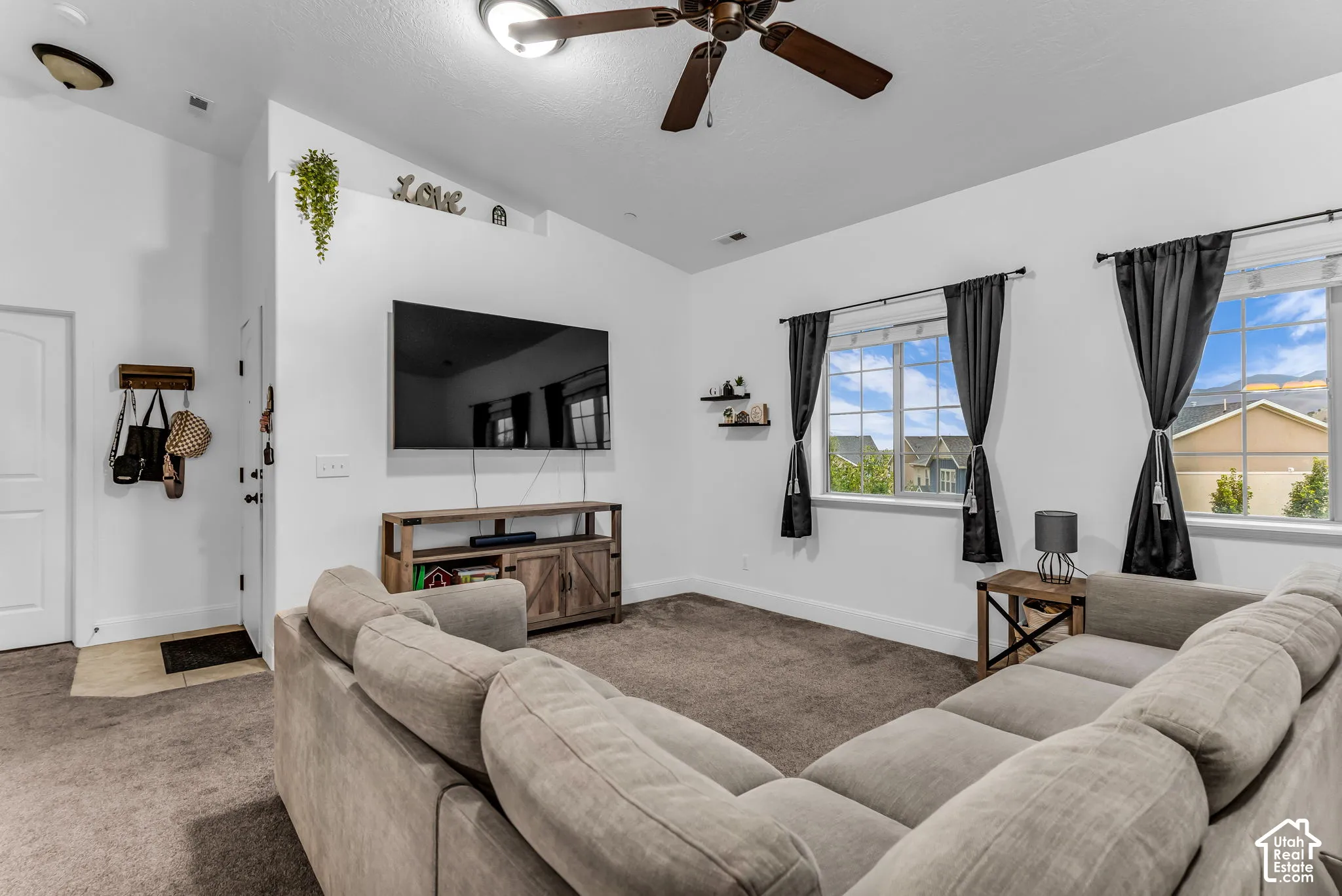 Vaulted ceiling, ceiling fan with integrated lighting, wood-finish media console, dual windows with gridded panes, and wall-mounted shelving