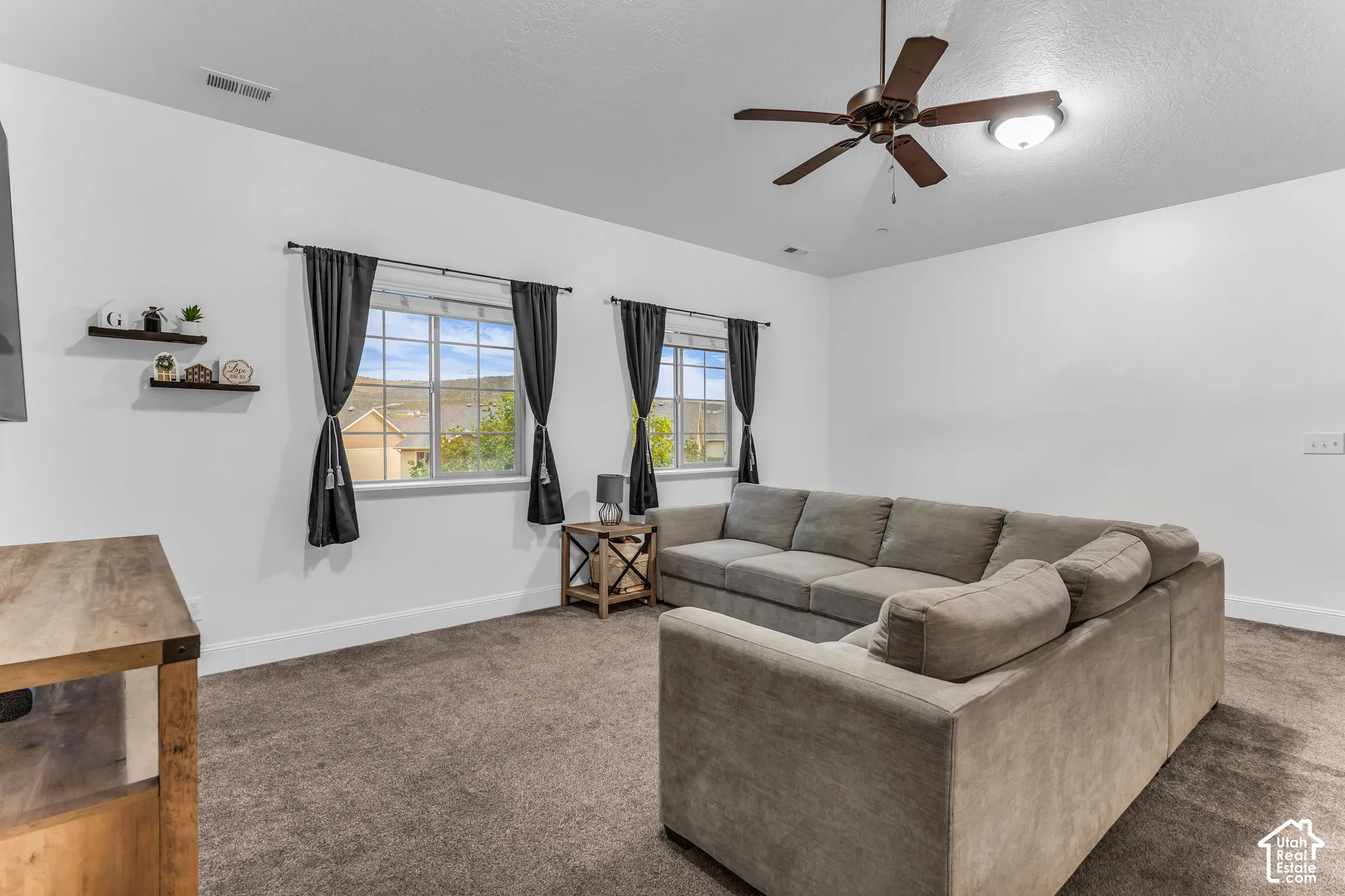 Two windows with dark drapery panels, textured carpeting, and a ceiling fan with integrated lighting