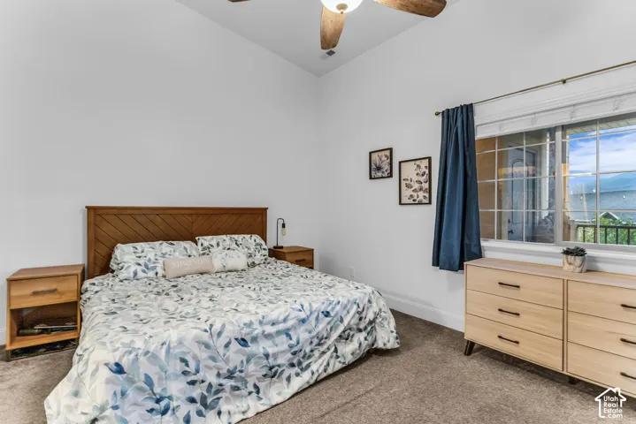 Angled wood headboard, wood-finish nightstands, vaulted ceiling, ceiling fan with light, and a window with white blinds