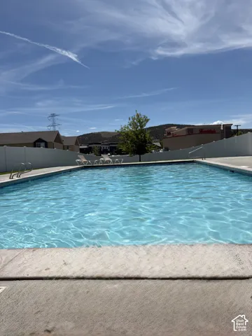Outdoor swimming pool with concrete decking, white privacy fencing, and distant hillside scenery