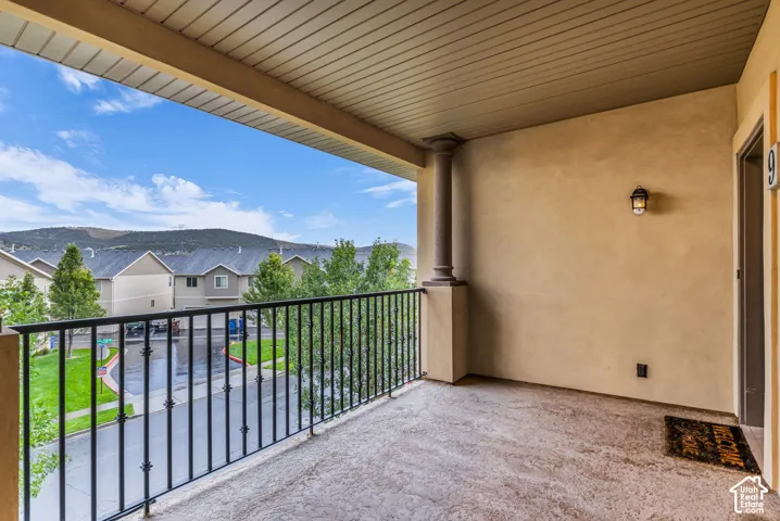Extended outdoor balcony featuring a decorative wrought iron railing, a classical-style column, and an exterior wall light fixture