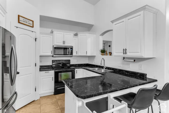 White cabinetry with crown molding, stainless steel microwave, black electric range, dark patterned countertops, and a dual-basin sink