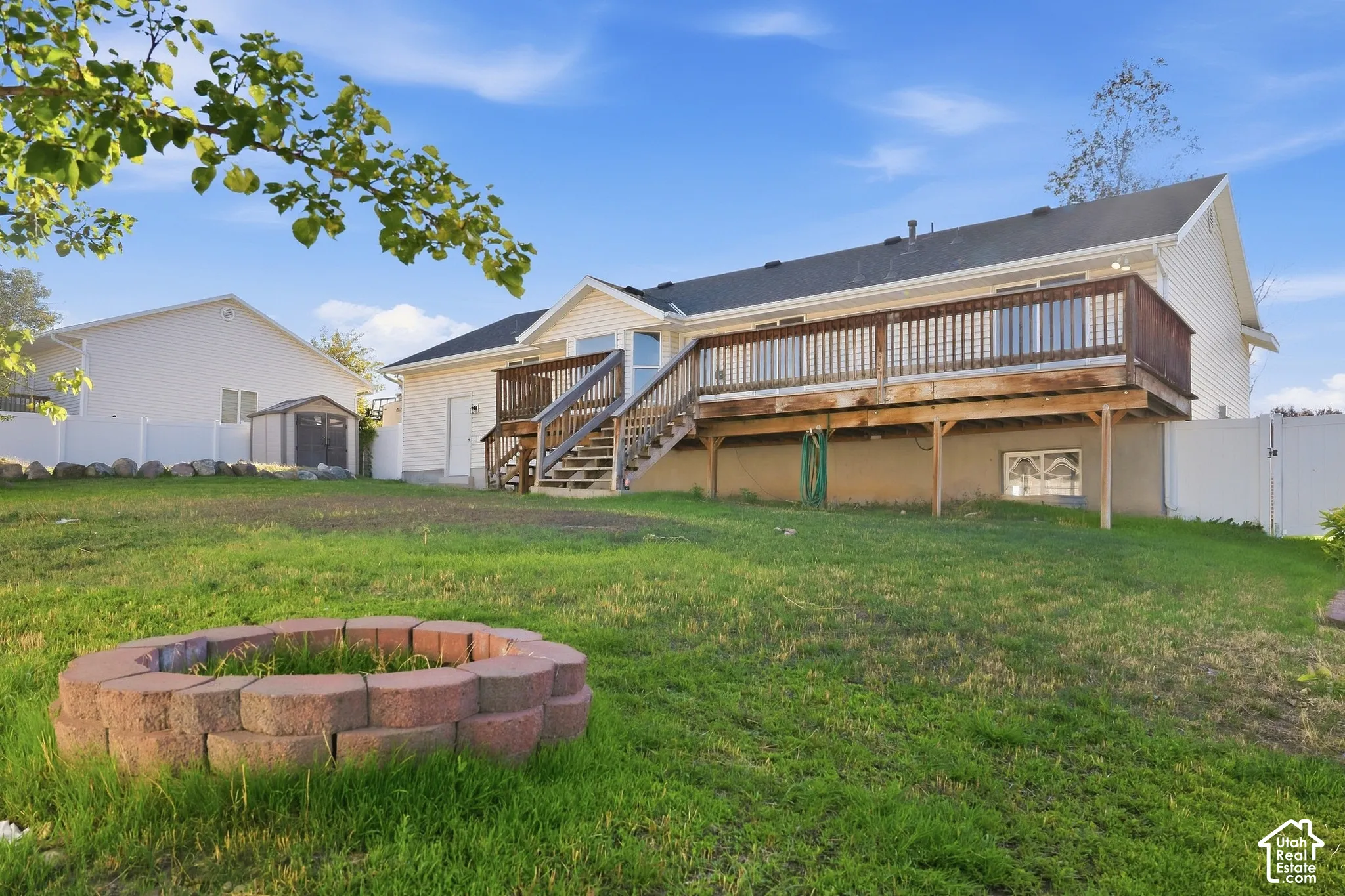 Expansive backyard featuring a built-in fire pit, a spacious wooden deck with railings, and a storage shed