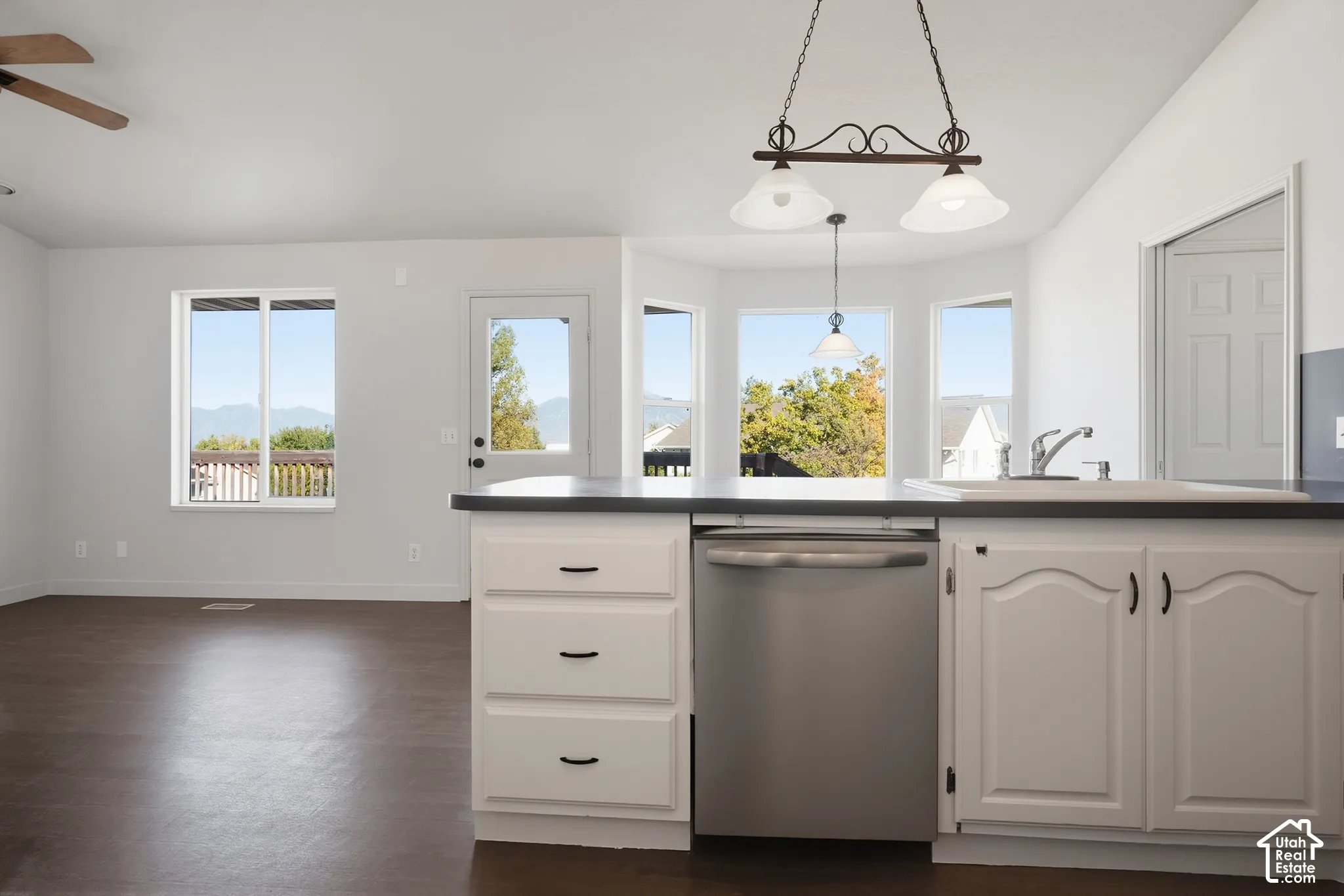 Kitchen island with white cabinetry and dark countertops, stainless steel dishwasher, and an integrated sink with a chrome faucet