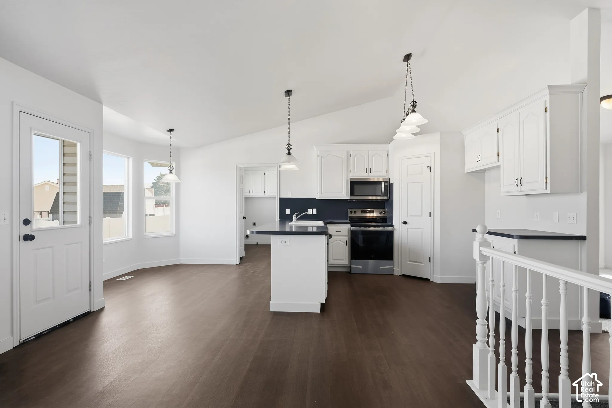 Open-concept kitchen with white cabinetry and dark countertops, stainless steel appliances, wood-finish flooring, and multiple pendant light fixtures