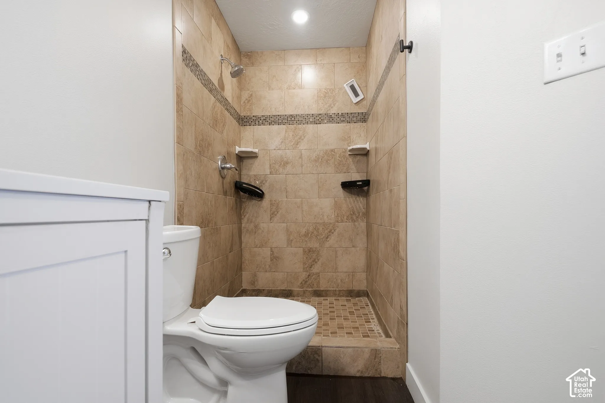 Tiled shower stall with a mosaic accent band, integrated shelving, and a showerhead