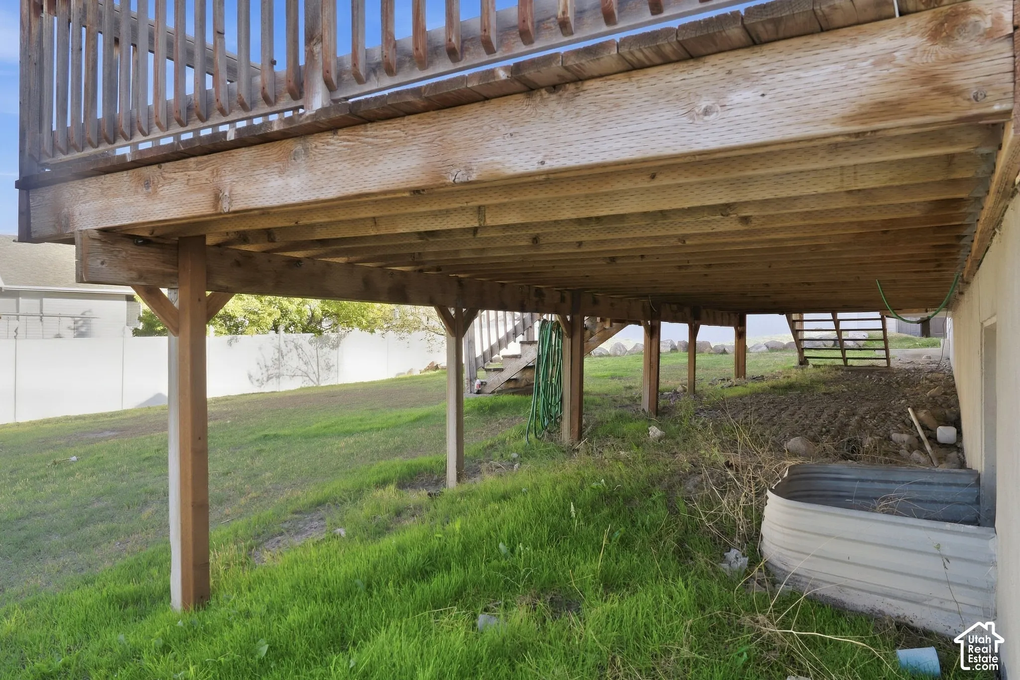 Elevated wood deck with baluster railing, supported by multiple wood posts, creating an under-deck area over a sloped grassy terrain