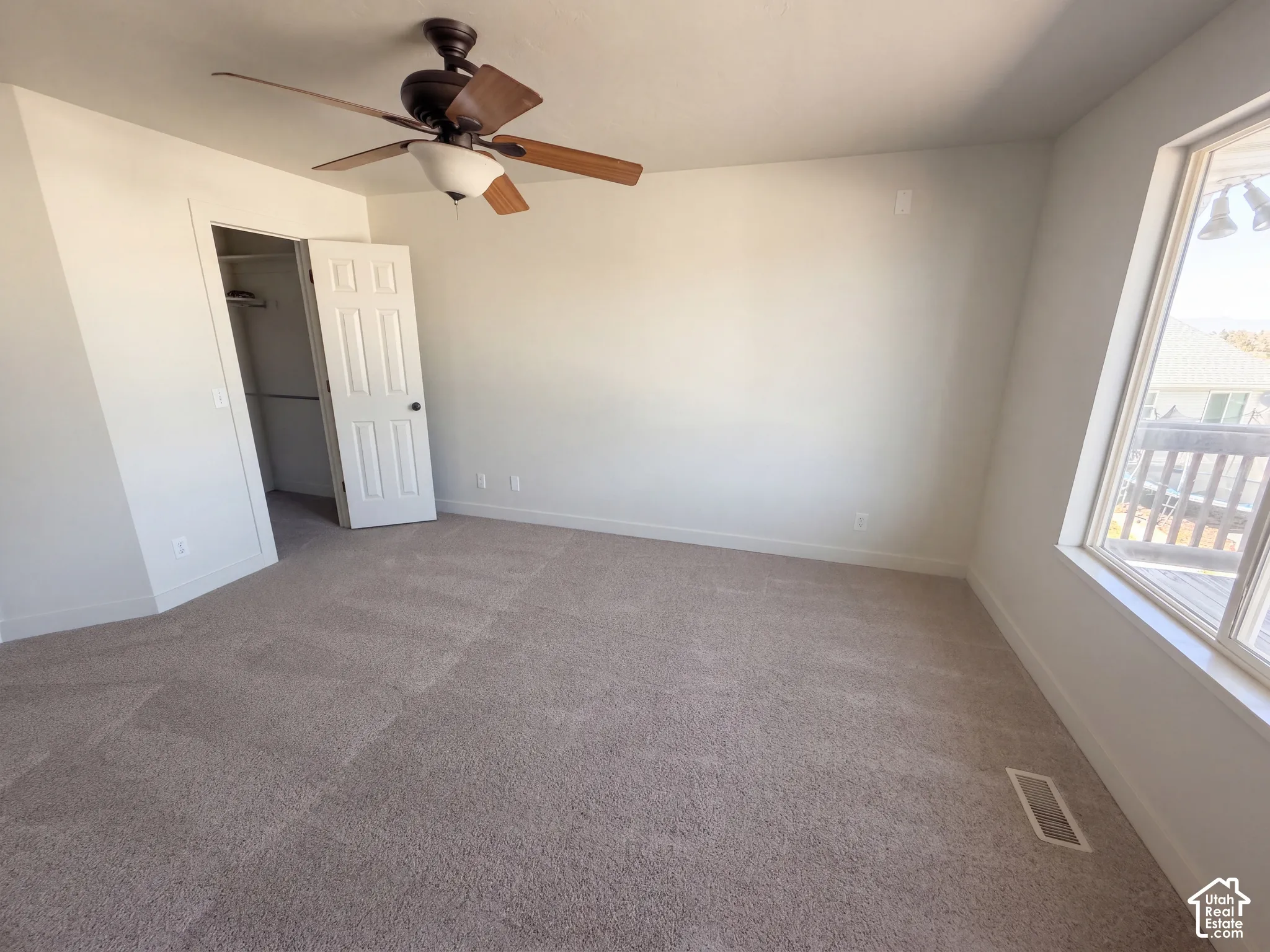 Spacious room featuring neutral carpeting, a ceiling fan with integrated lighting, and a window providing natural illumination