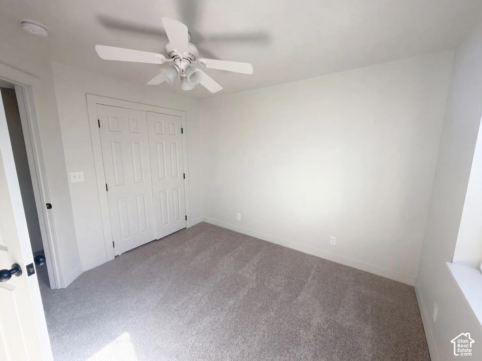 Neutral wall color, ceiling fan with integrated lighting, textured carpet flooring, bi-fold closet doors, and natural light from the window