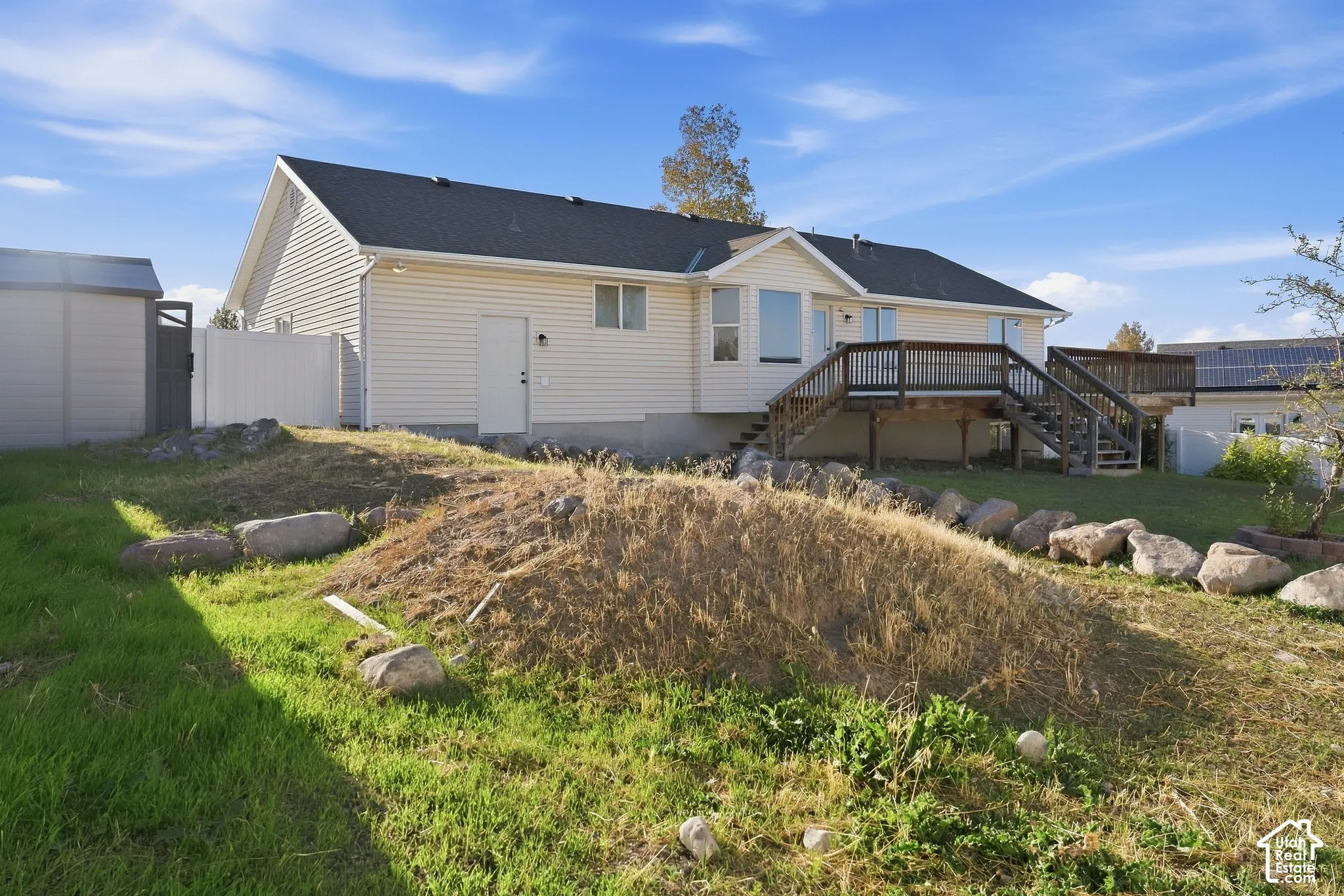 Exterior featuring light-colored siding, a dark shingle roof, an elevated wood deck with railings, and a white privacy fence
