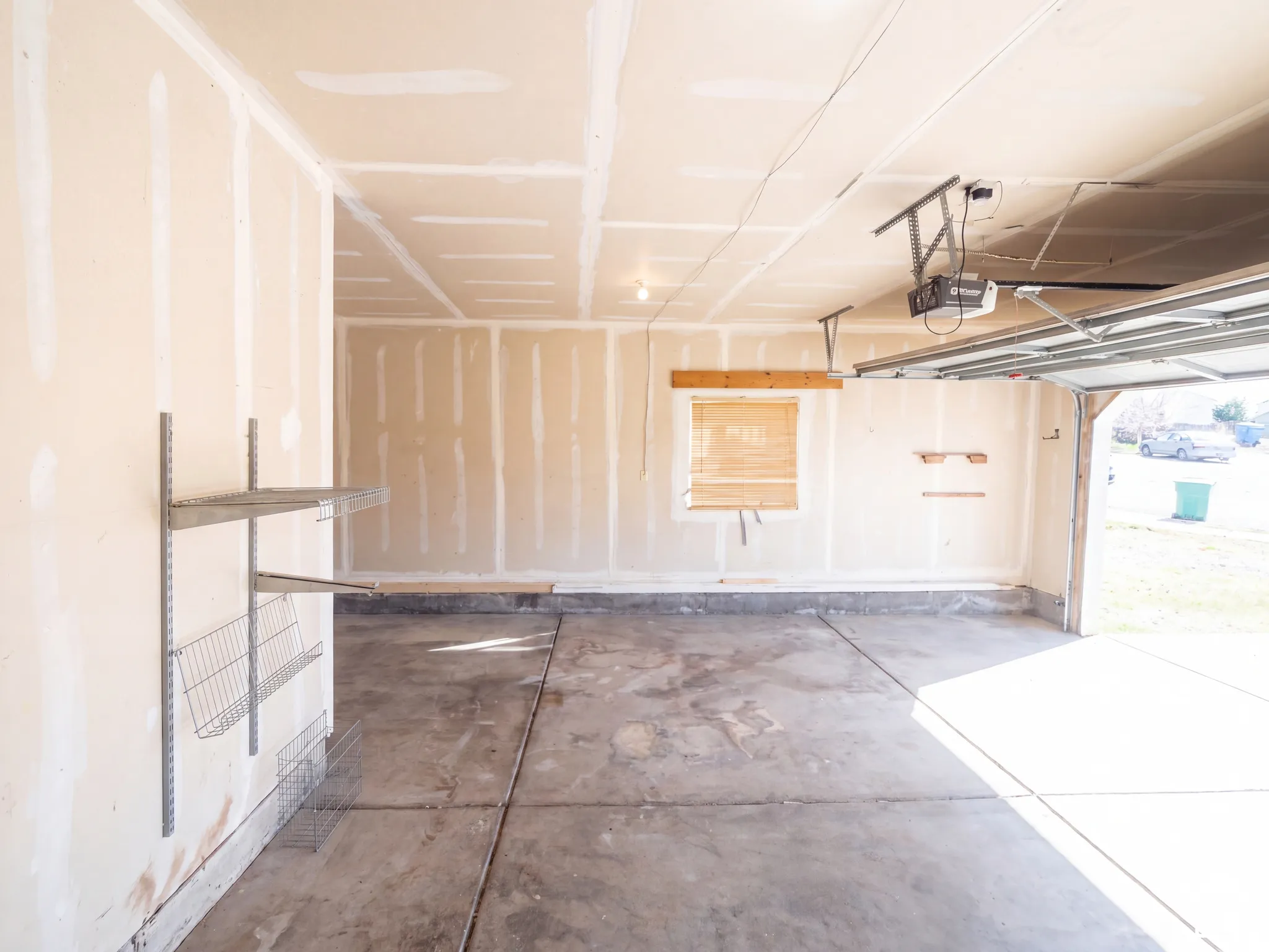Attached garage with an overhead garage door opener, concrete flooring, and wall-mounted shelving