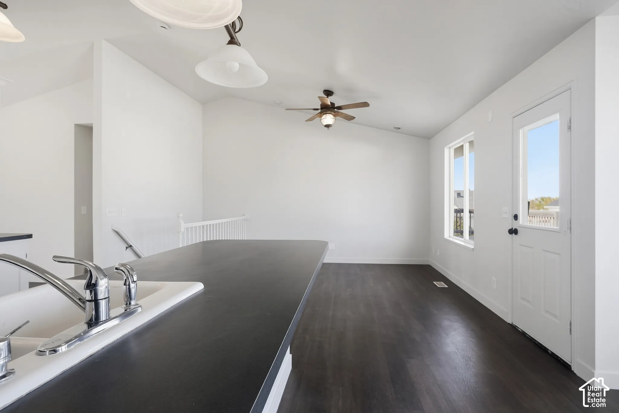 Sleek countertop with an integrated sink and chrome faucet, dark wood-finish flooring, white walls, ceiling fan, and a door with an exterior window