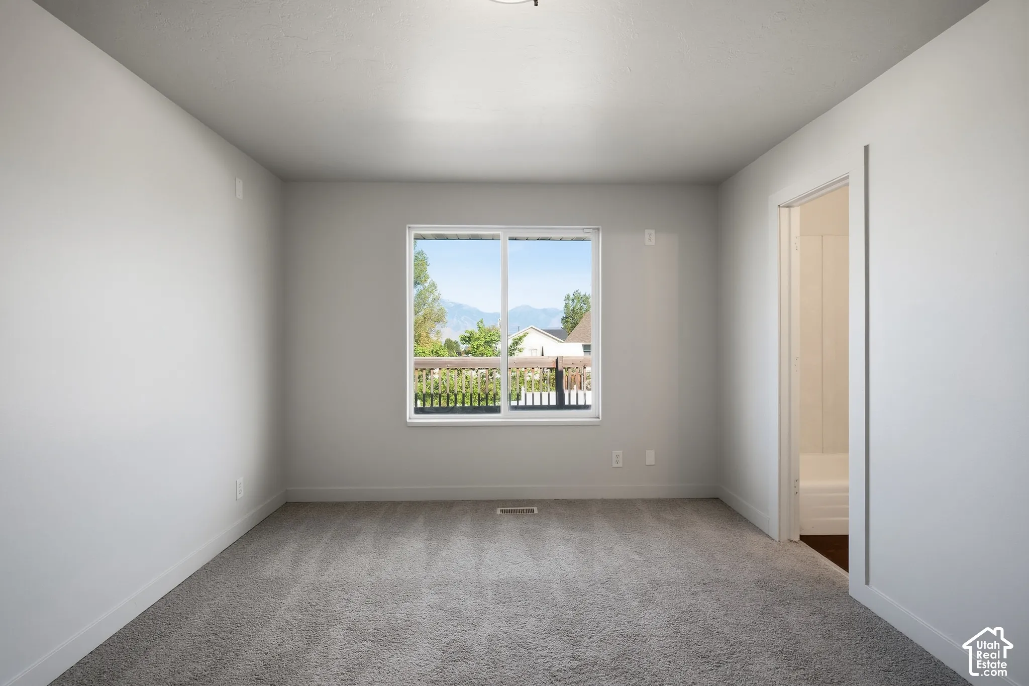 Neutral wall paint, gray carpet flooring, window with white trim, white door frame, and a ceiling-mounted light fixture