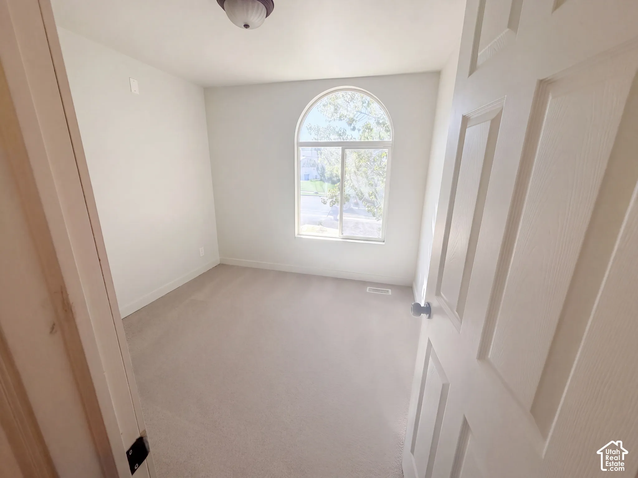 Arched window with light-toned trim, light-toned carpeting, and a flush-mount ceiling light fixture
