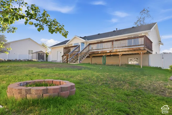 Expansive backyard featuring a built-in fire pit, a spacious wooden deck with railings, and a storage shed