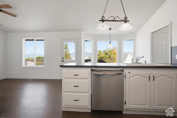 Kitchen island with white cabinetry and dark countertops, stainless steel dishwasher, and an integrated sink with a chrome faucet