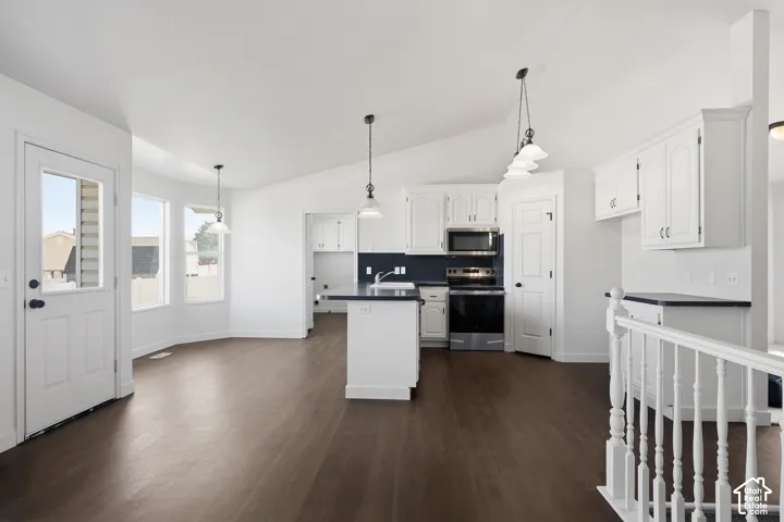 Open-concept kitchen with white cabinetry and dark countertops, stainless steel appliances, wood-finish flooring, and multiple pendant light fixtures