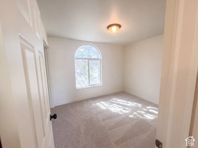 Arched window with clear glass, light-colored carpet flooring, flush-mount ceiling light fixture, white interior walls, and white paneled door