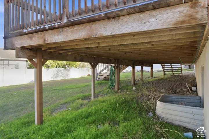 Elevated wood deck with baluster railing, supported by multiple wood posts, creating an under-deck area over a sloped grassy terrain