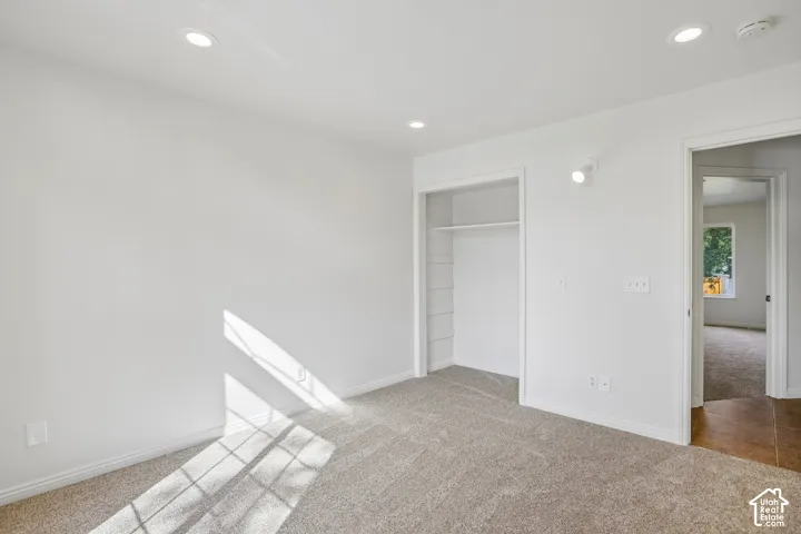 White walls, recessed ceiling lighting, light-toned carpet, and a built-in closet with shelving and hanging rod