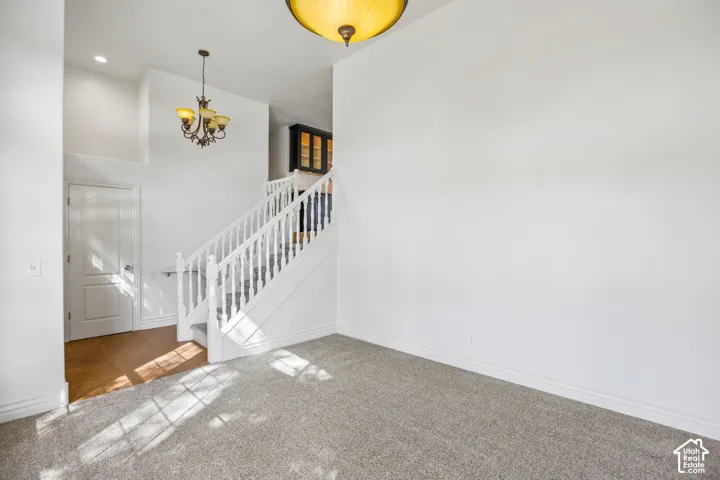 Carpeted flooring, high ceilings, traditional chandelier, white staircase with balusters, and wood-finish flooring