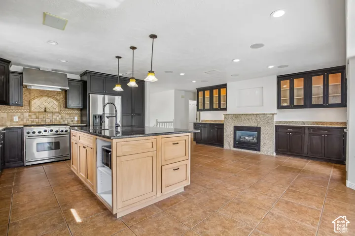 Spacious kitchen featuring an expansive center island, stainless steel range with hood, tiled backsplash, built-in fireplace, and integrated cabinetry