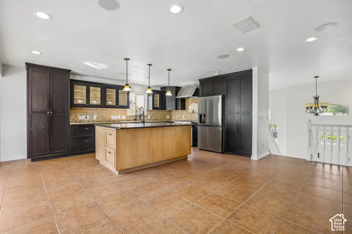 Kitchen featuring dark wood cabinetry, a light wood-finish island, stainless steel appliances, and a tiled backsplash