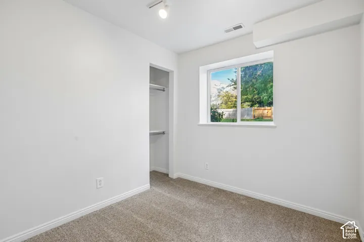 Wall-to-wall carpeting, window with outdoor scenery, recessed closet with shelving, track lighting, and a wall-mounted climate control unit