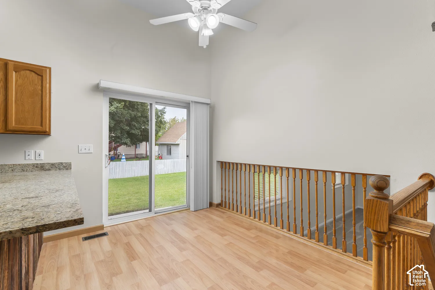 Vaulted ceiling, wood-finish flooring, sliding glass door, wooden staircase railing, and ceiling fan with integrated lighting