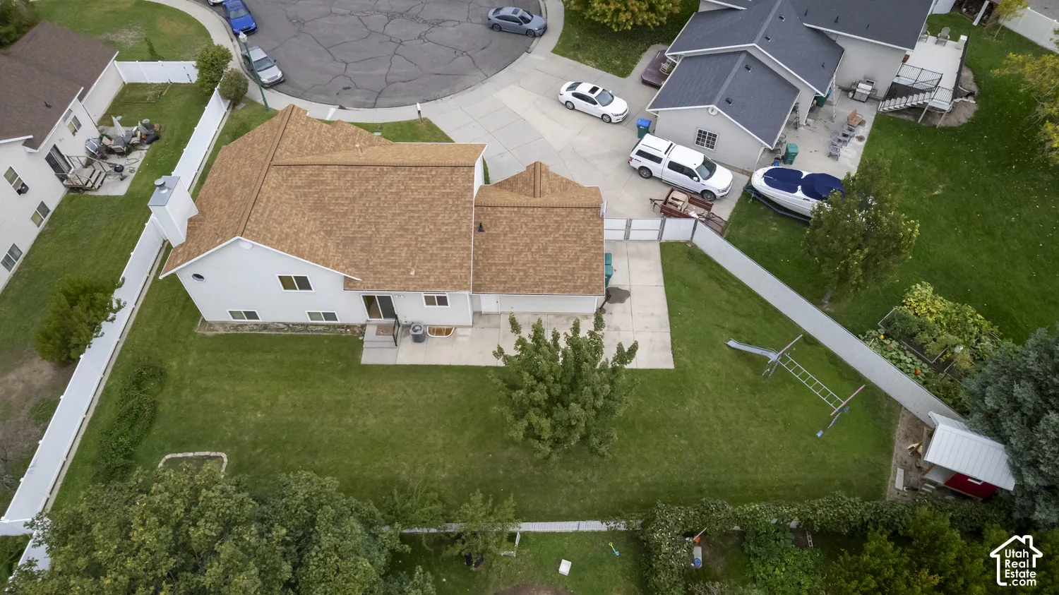 Expansive green lawn with mature landscaping, white privacy fence, and concrete patio