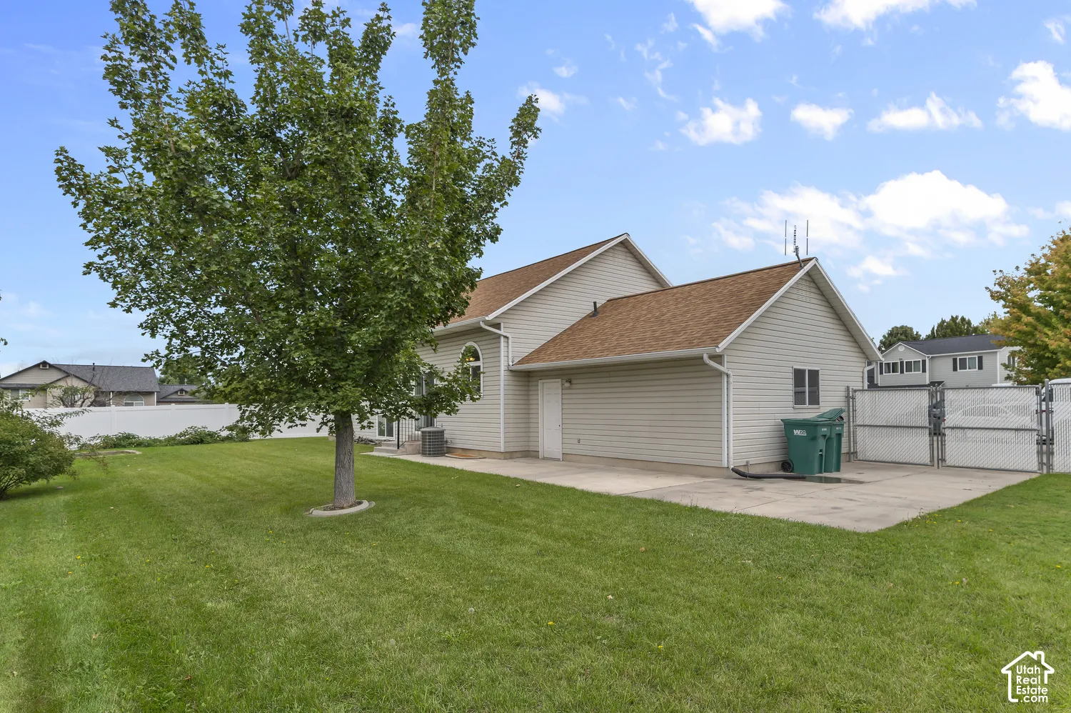 Expansive green lawn, mature shade tree, concrete patio, chain-link fencing, and light-colored siding
