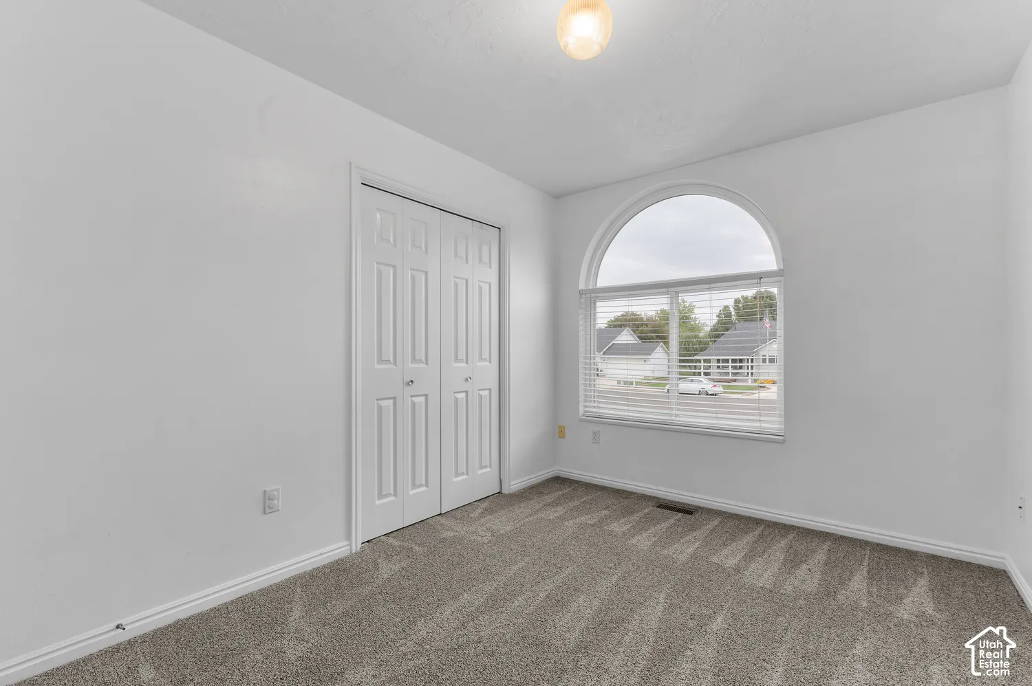 Arched window with blinds, bi-fold closet doors, wall-to-wall carpeting, and a ceiling-mounted light fixture