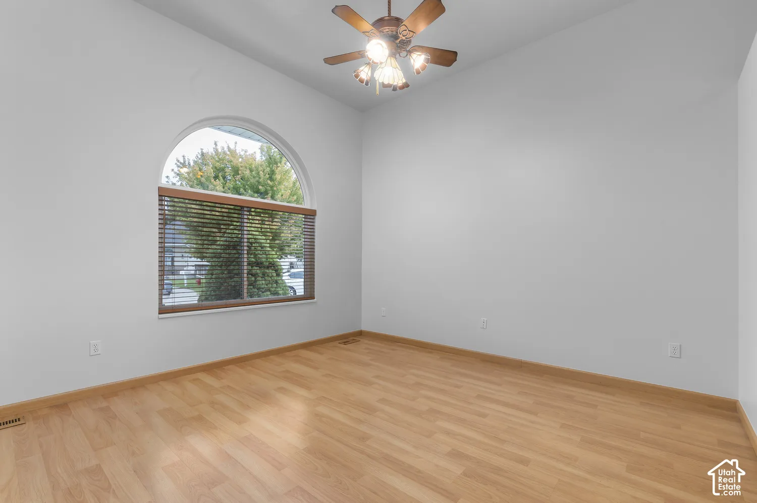 Arched window with wooden blinds, wood-finish flooring, and a ceiling fan fixture