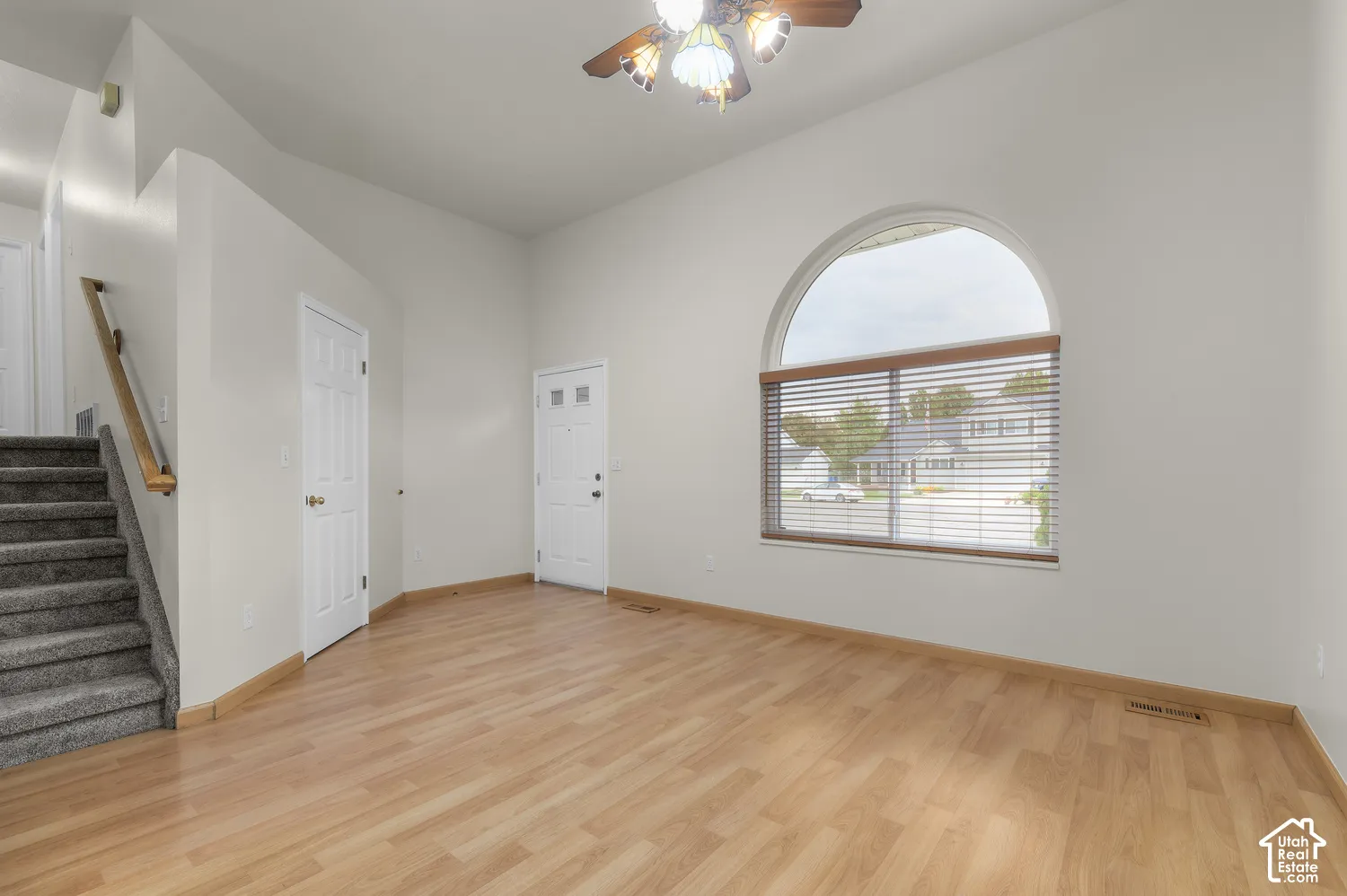 Vaulted ceiling with a decorative ceiling fan, arched window with wood blinds, wood-finish flooring, and a carpeted staircase