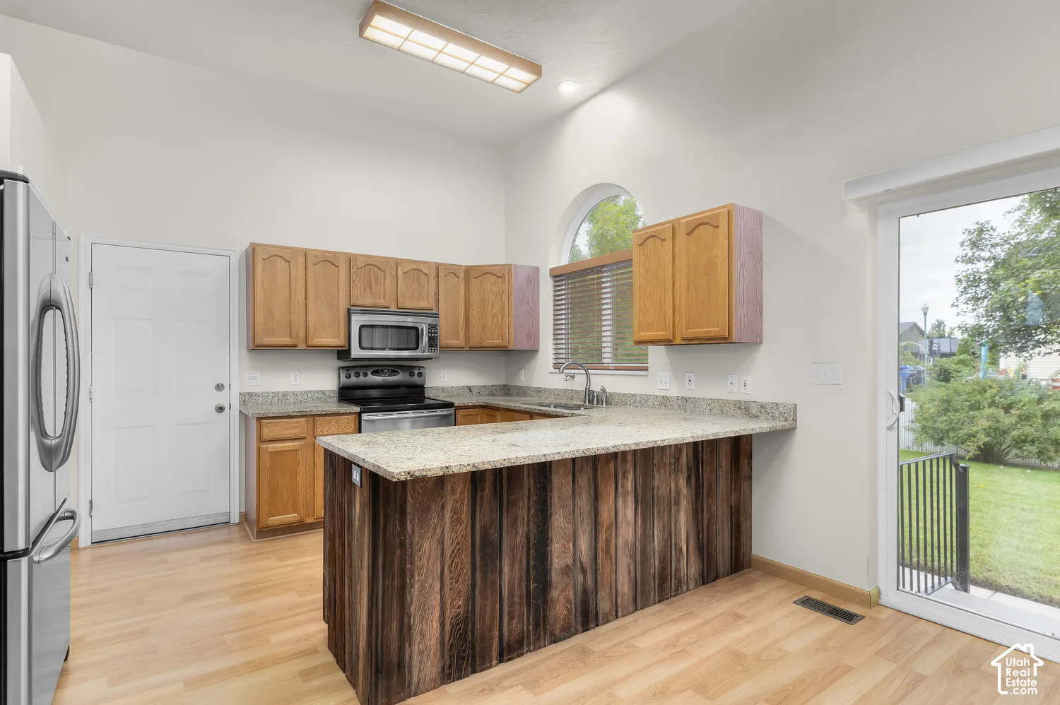 Kitchen featuring wood-finish flooring, light wood cabinetry, stainless steel appliances, and a breakfast bar with a textured wood-panel base