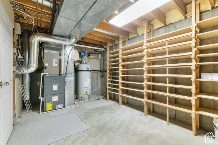 Utility room featuring a water heater, furnace, and extensive built-in wooden shelving for ample storage