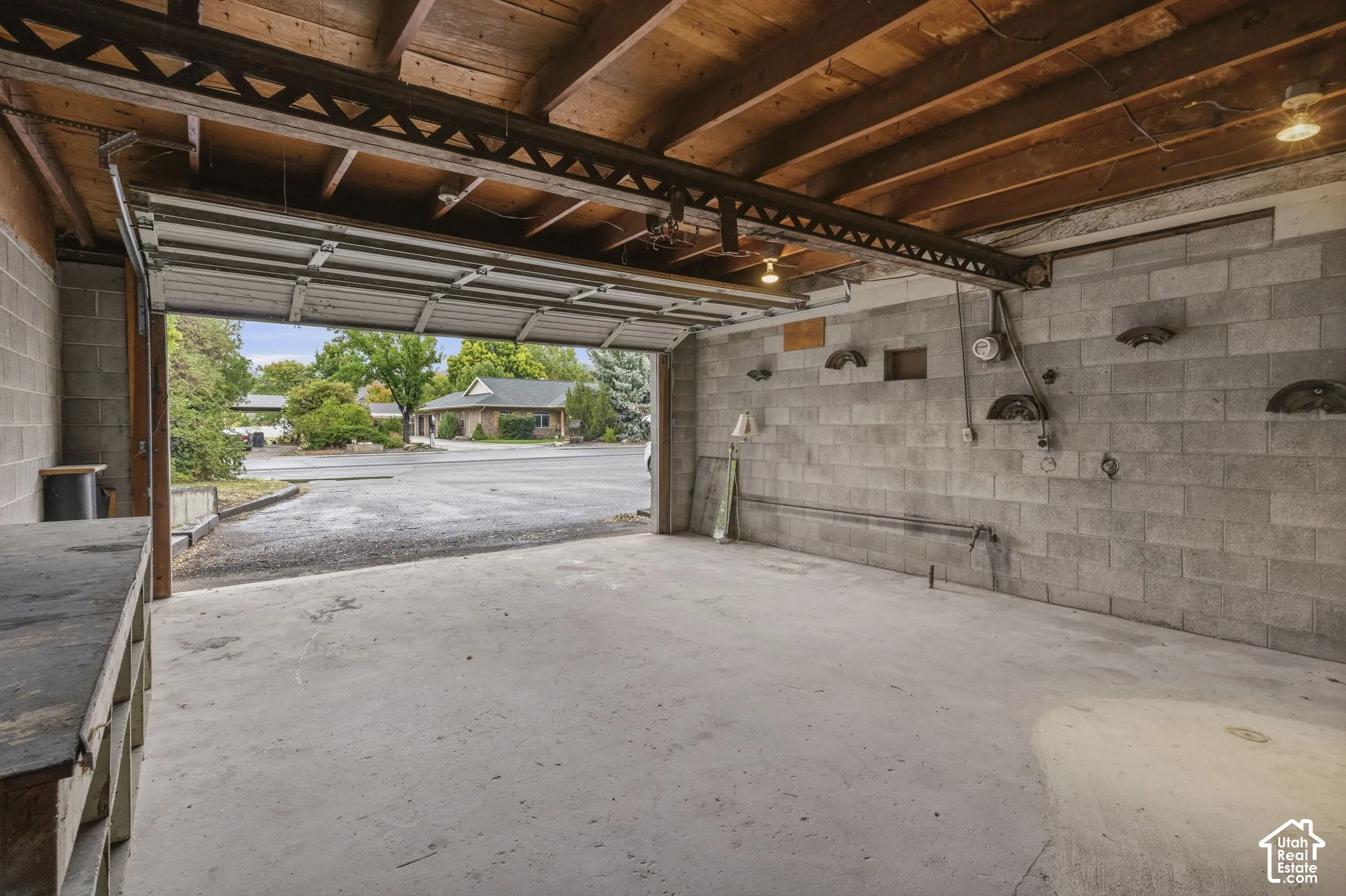 Garage attached to Detached Building - Concrete block walls with exposed wood beam ceiling, concrete floor, and an open manual garage door. Bridge beam for engine hoist