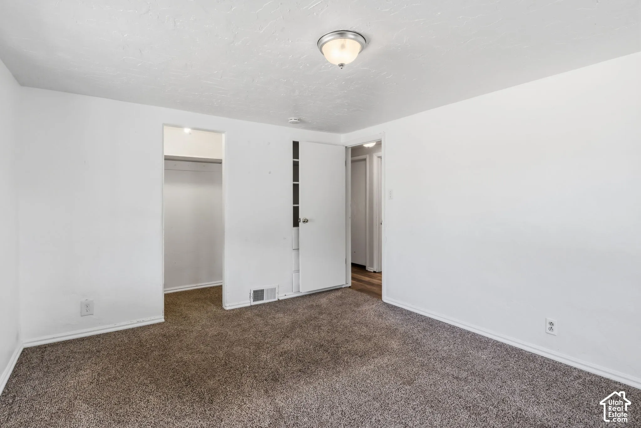 Carpeted flooring, white painted walls, and a semi-flush mount ceiling light, built in drawers and shelves behind bedroom door